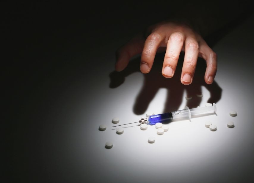 Drug abuse awareness image with hand reaching for syringe and pills