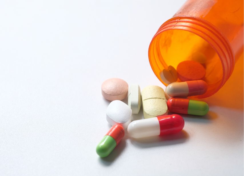 Prescription pills and capsules spilled from orange pill bottle on white background