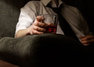 Man in a dress shirt and tie sitting in an armchair, holding a glass of whiskey