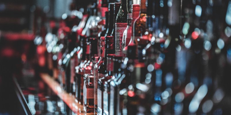 Rows of assorted liquor bottles lined up on a bar counter in low light