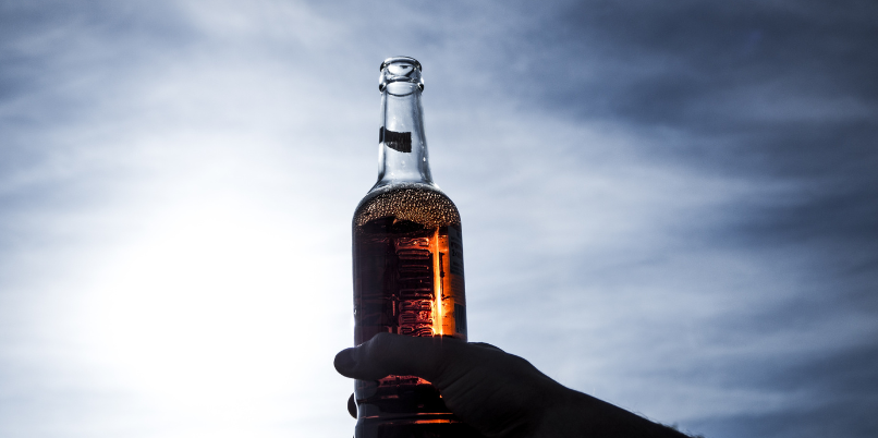 Hand holding a bottle of beer up to the sky with sunlight shining through the glass