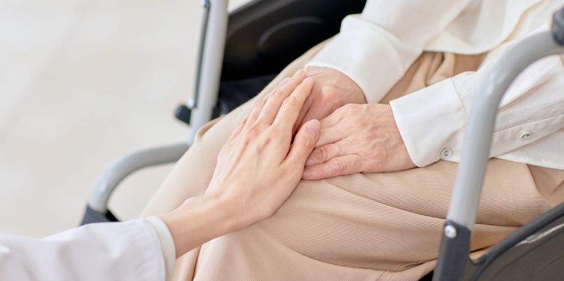 Close-up of a comforting hand placed gently on the hands of an elderly person sitting in a wheelchair
