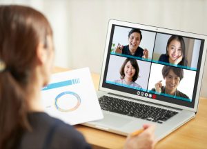 Person attending an online group meeting via video call on a laptop, holding a presentation document